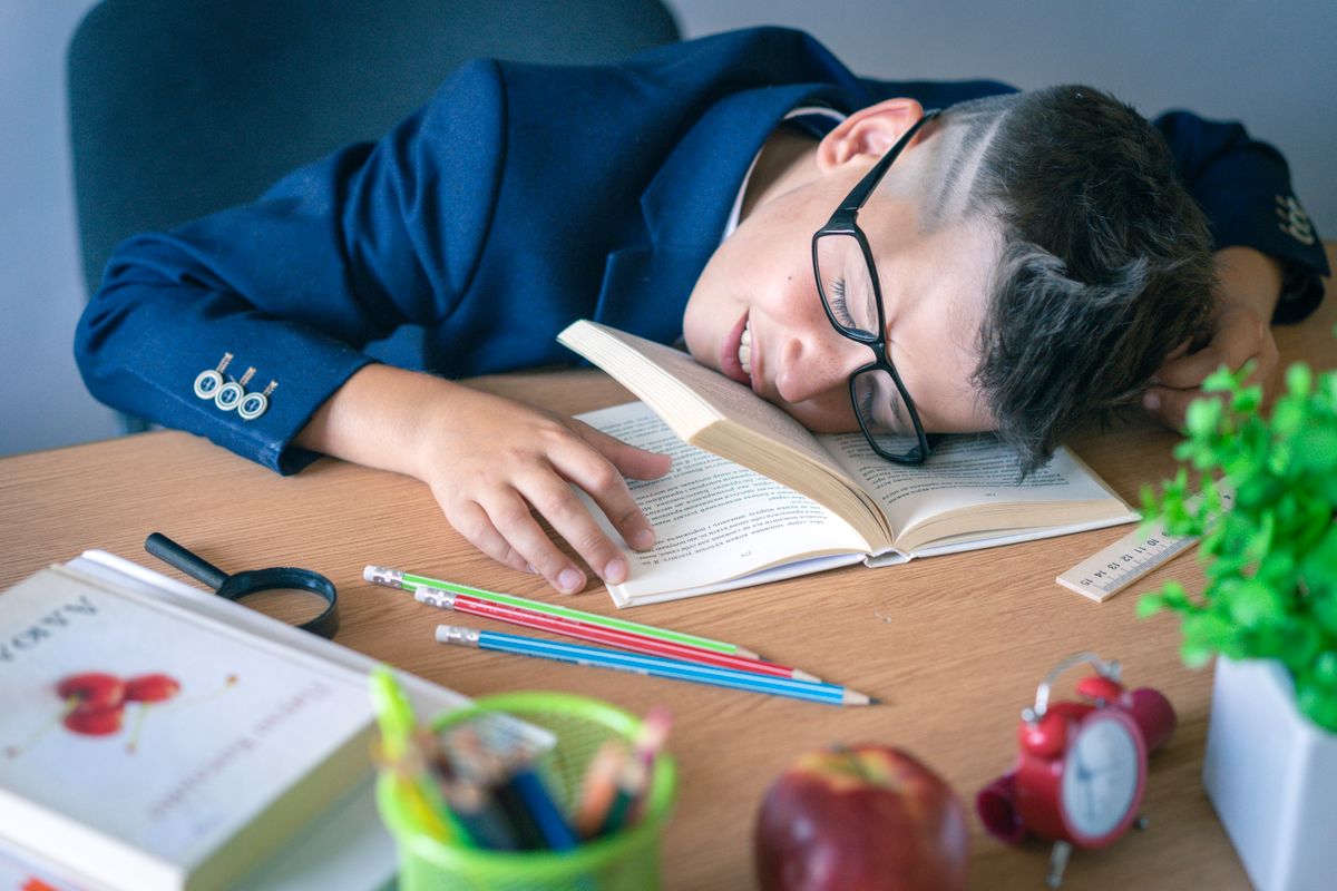 A tired schoolboy in glasses sleeping on a desk surrounded by study materials. A tired schoolboy in glasses sleeping on a desk surrounded by study materials.