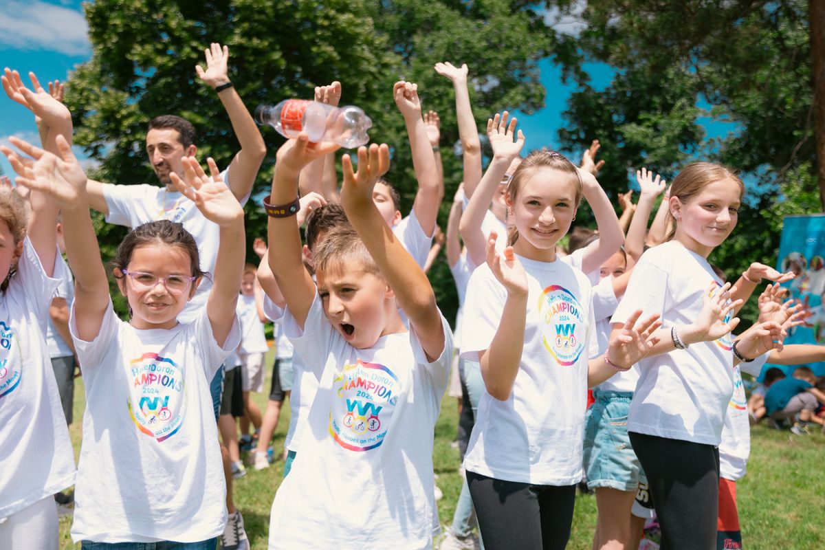 Group of cheerful children raising hands in a park during a sunny day, wearing t-shirts with event logos. - Photo by Aleksandar Andreev on Pexels