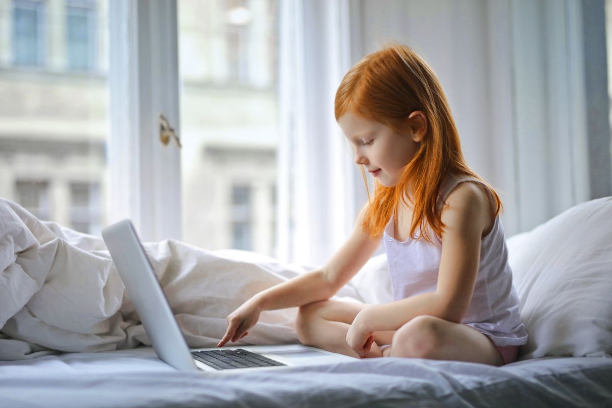 Redheaded girl sits on bed using laptop in a sunlit bedroom, enjoying leisure time. - Photo by Andrea Piacquadio on Pexels