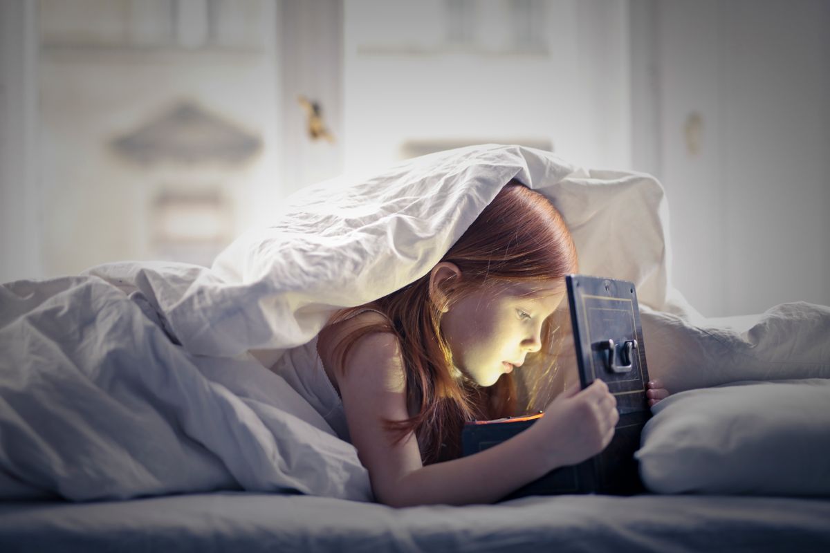 A young girl with red hair explores a glowing box under a blanket indoors. - Photo by Andrea Piacquadio on Pexels
