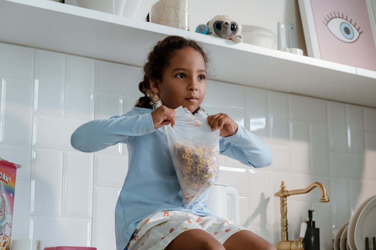 Young girl sitting in kitchen holding cereal bag, ready for breakfast. - Photo by cottonbro studio on Pexels