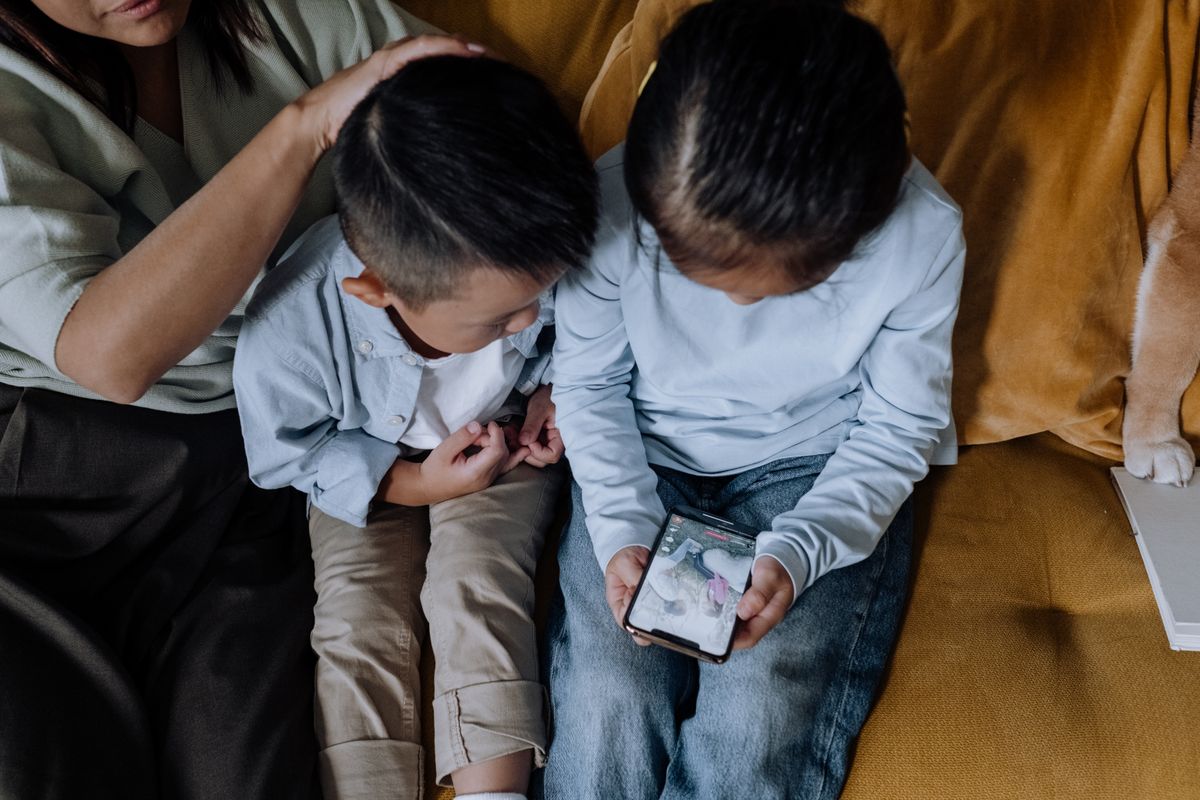 Two kids sharing a smartphone while sitting with family on a cozy couch. - Photo by cottonbro studio on Pexels