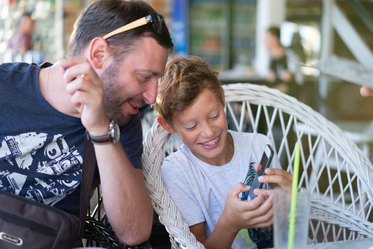 Father and son bonding over a smartphone, sharing a joyful moment in a cozy cafe. Father and son bonding over a smartphone, sharing a joyful moment in a cozy cafe.