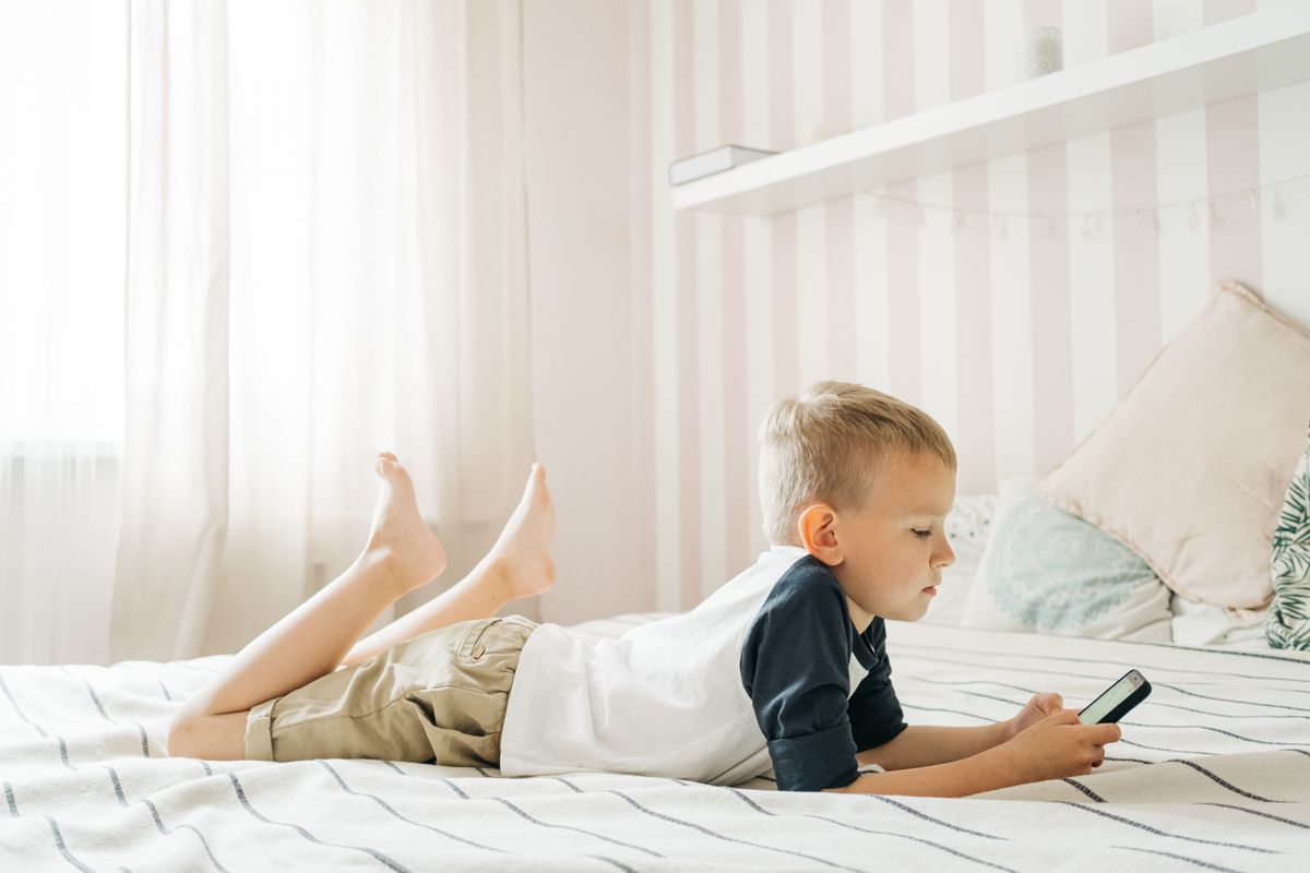 Young boy lying on bed using smartphone in a bright room, enjoying leisure time. - Photo by Ivan S on Pexels