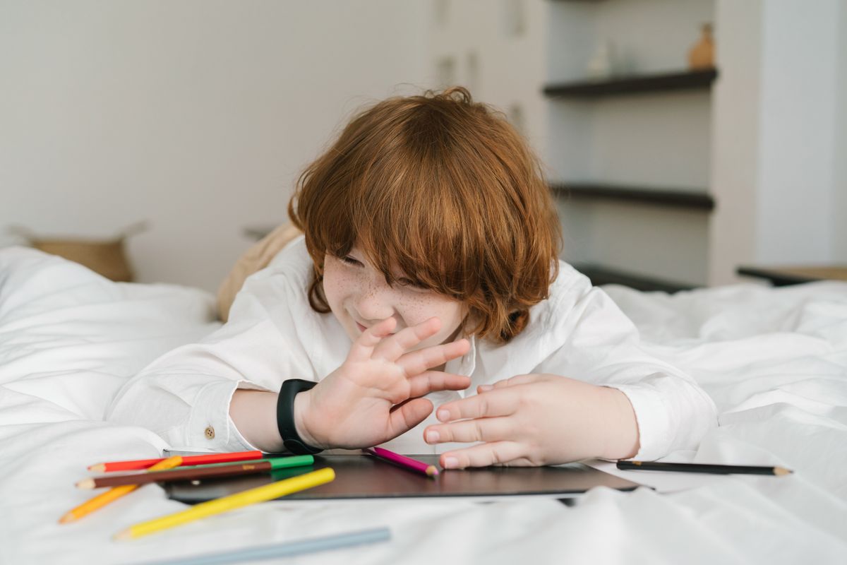 A young redheaded boy lying on a bed, playing with colored pencils indoors, expressing creativity. - Photo by Mikhail Nilov on Pexels