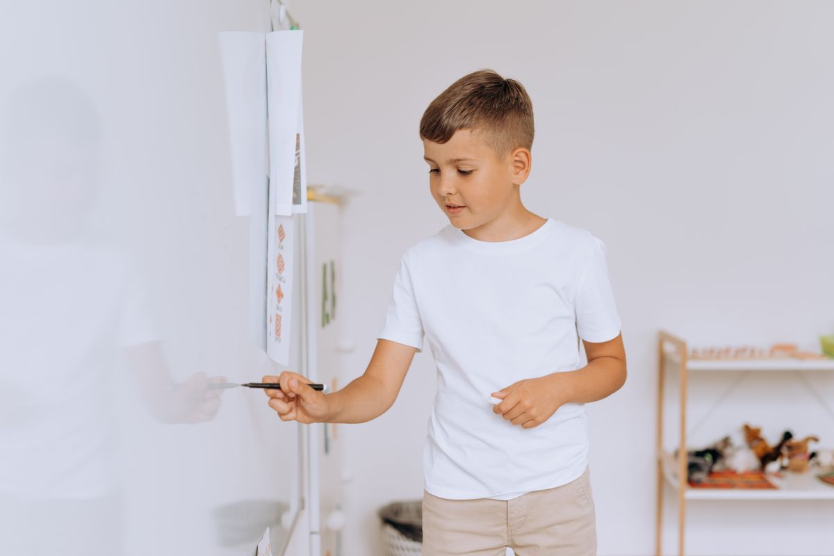Child in a classroom setting writing on a whiteboard, focusing on education and learning. - Photo by Mikhail Nilov on Pexels