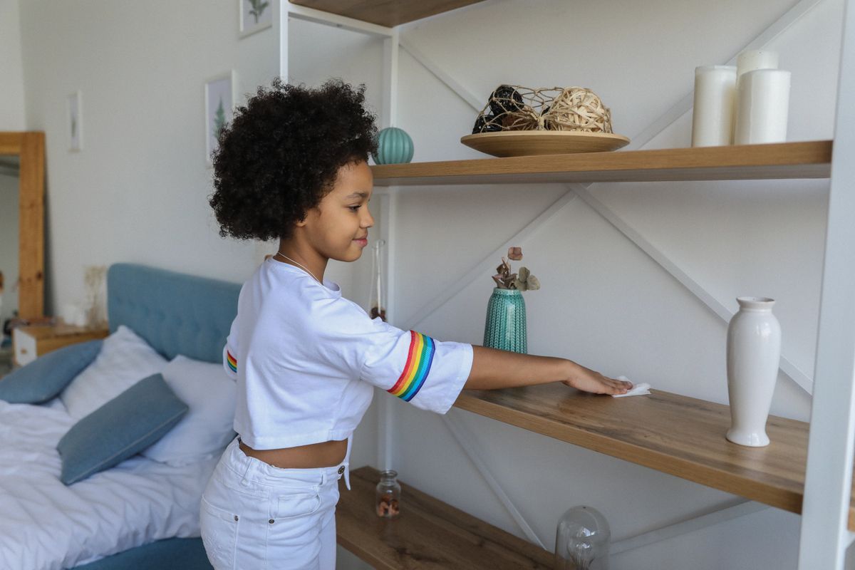 Charmantes afroamerikanisches Mädchen wischt zu Hause Staub vom Holzregal eines Regals – Foto von Monstera Production auf Pexels