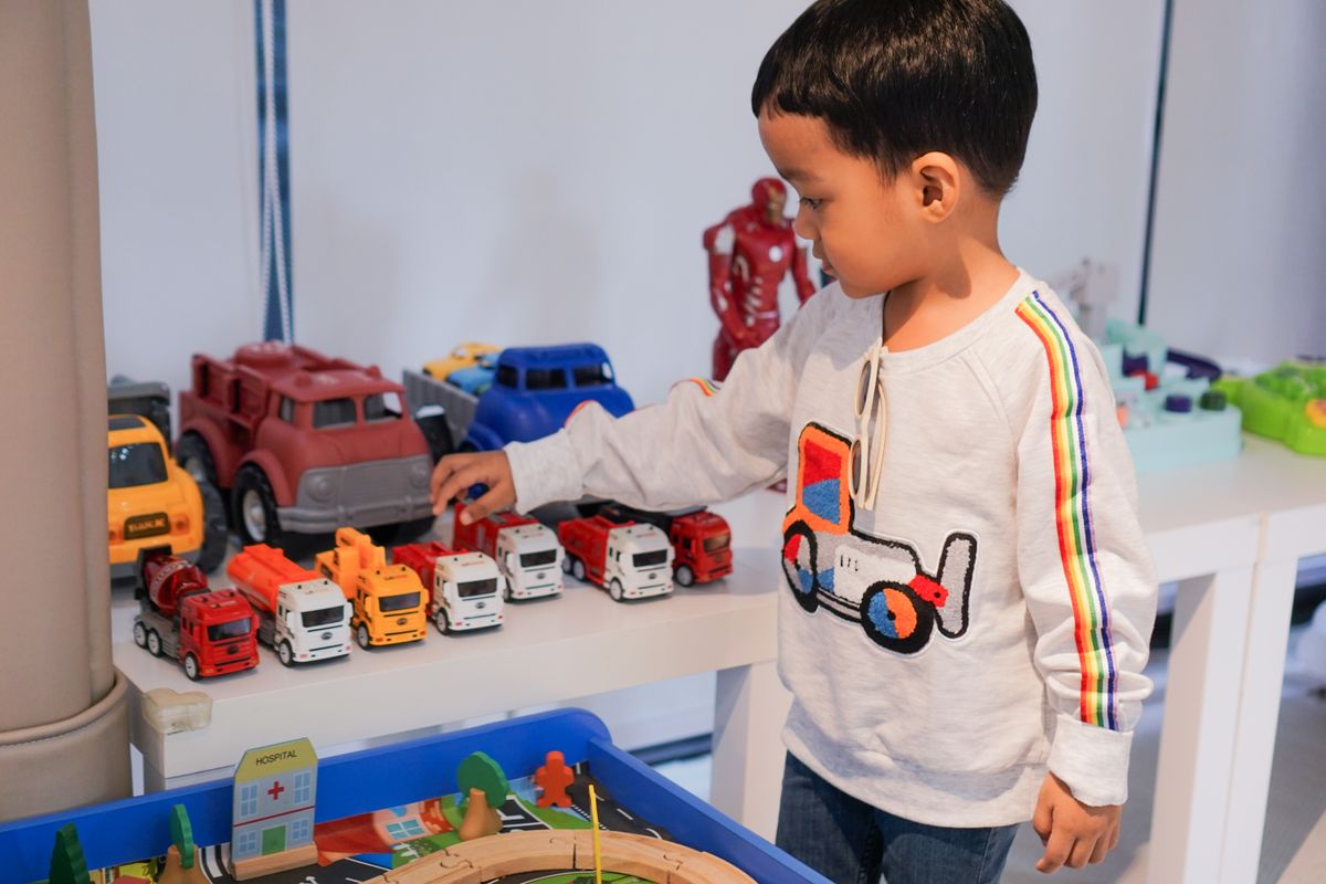 A young boy playing indoors with colorful toy trucks on a table, focused and imaginative. - Photo by pipop kunachon on Pexels