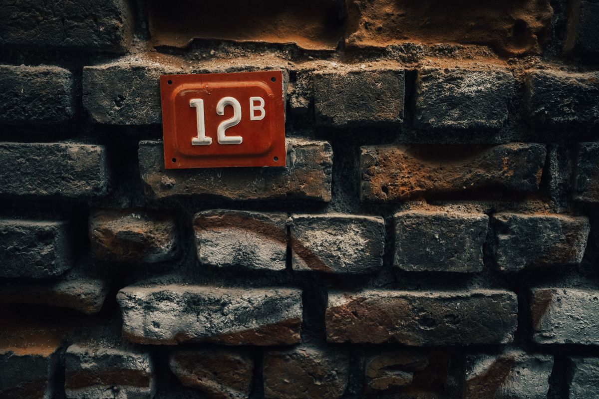 Close-up of a vintage red number plate '12B' mounted on a rustic brick wall. - Photo by Sami  Aksu on Pexels