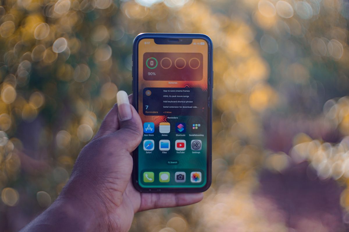 A hand holding a smartphone showing home screen apps, outdoors with bokeh background. - Photo by Soundarapandian MS on Pexels