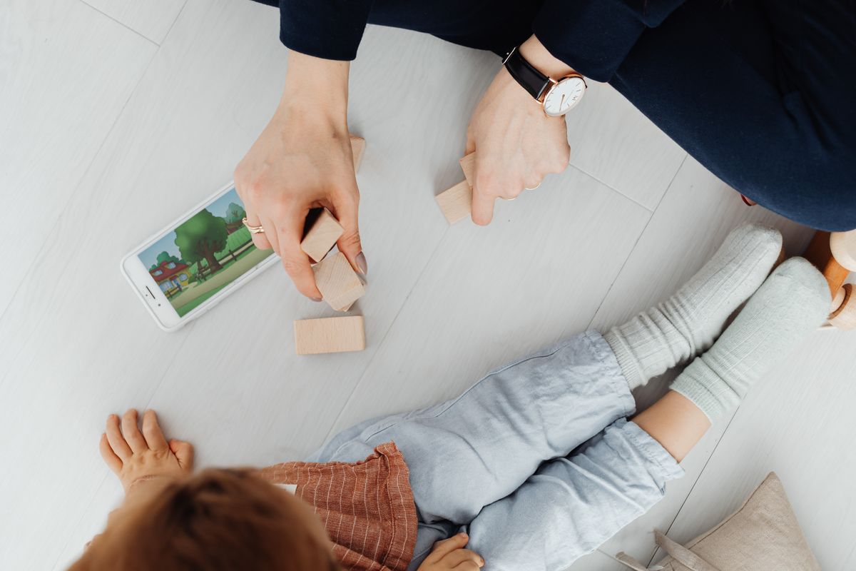 A mother and child playing with wooden blocks and a smartphone on the floor. - Photo by www.kaboompics.com on Pexels