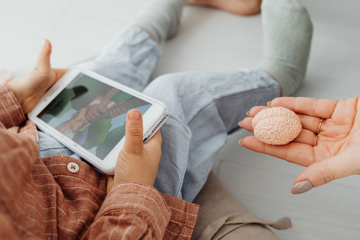 A child watches a cartoon on a tablet as an adult holds a brain model. - Photo by www.kaboompics.com on Pexels