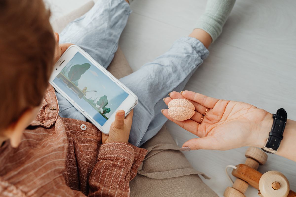 Young child engrossed in a smartphone video while holding a brain model indoors. - Photo by www.kaboompics.com on Pexels
