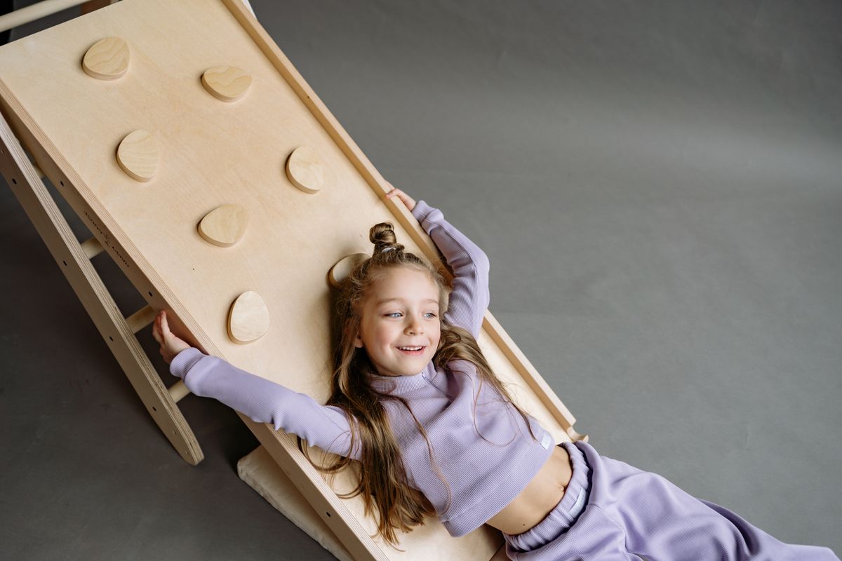 A joyful child enjoying playtime on a wooden climbing frame indoors. - Photo by Yan Krukau on Pexels