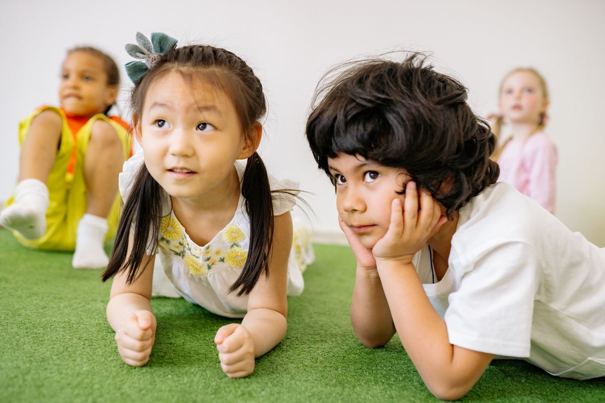 Group of children lying on grass indoors, enjoying a playful learning activity in kindergarten. - Photo by Yan Krukau on Pexels